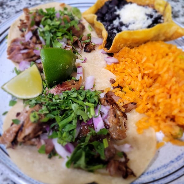 Mucho Bueno Street Food & Tequila's carne asada tacos with rice and black beans on a plate.