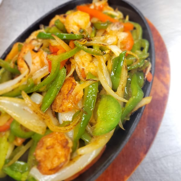 Sizzling shrimp fajitas with green peppers, onions, and carrots in a black skillet on a wooden board.