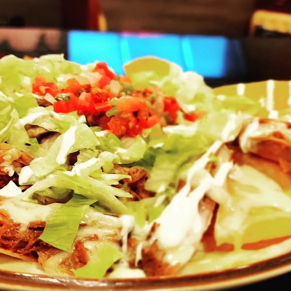 Close-up of Mucho Bueno Street Food & Tequila's Mexican dish with meat, lettuce, pico de gallo, and crema.
